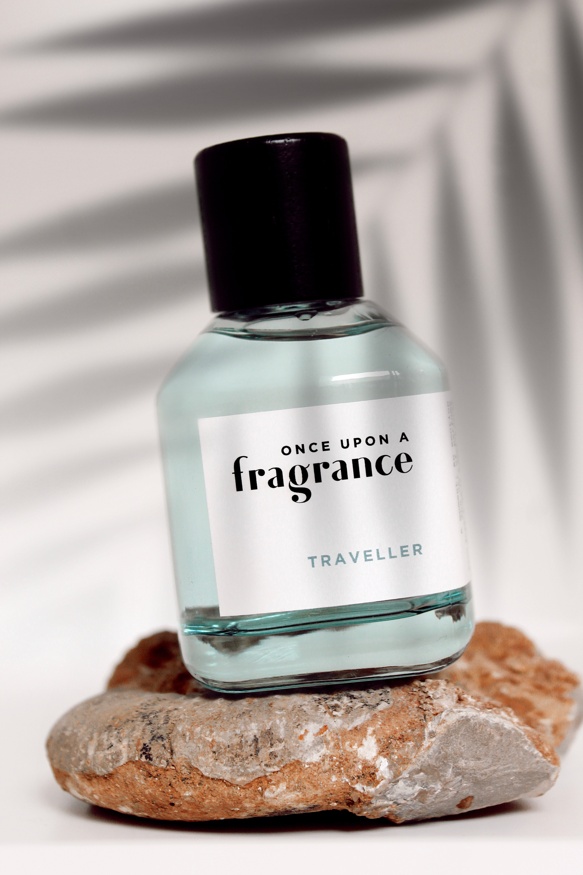 TRAVELLER fragrance bottle by Once Upon a Fragrance on a rock next to a palm tree shadow, showcasing a premium, long-lasting French perfume with exotic spices and woody notes